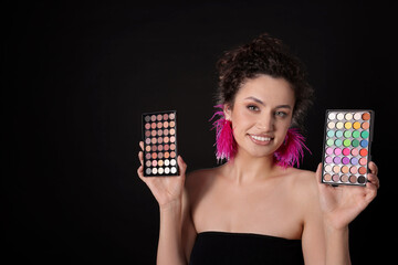Smiling woman with eyeshadow palettes on black background. Space for text