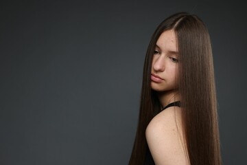 Beautiful teenage girl with healthy long hair on dark grey background. Space for text