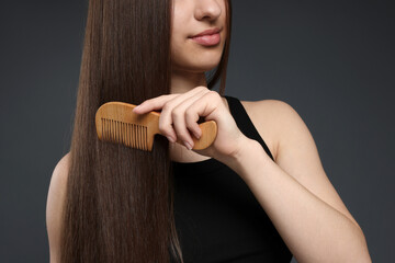 Teenage girl brushing her healthy long hair on dark grey background, closeup