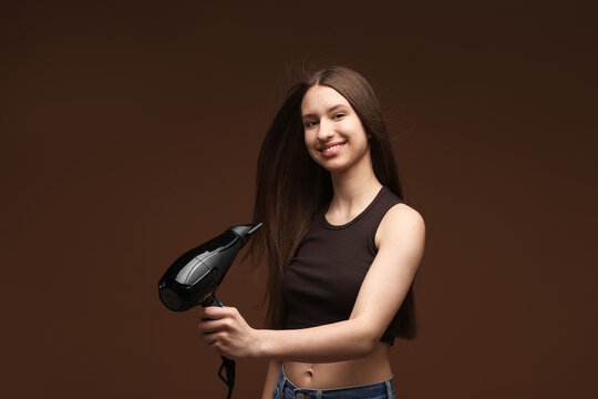 Fototapeta Smiling teenage girl with hair dryer on brown background