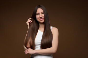 Portrait of smiling teenage girl with healthy long hair on brown background