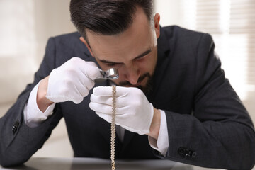 Appraiser evaluating luxury necklace at table indoors