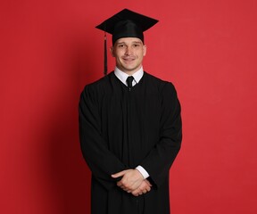 Happy student after graduation on red background
