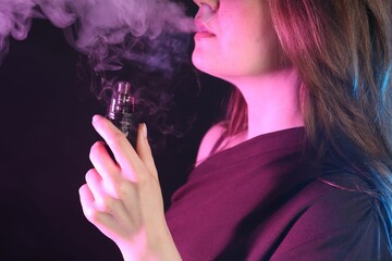 Woman using electronic smoking device in neon lights on black background, closeup