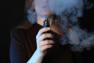 Woman using electronic smoking device on black background, closeup