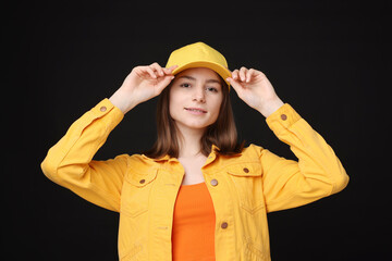 Young woman wearing stylish yellow baseball hat on black background