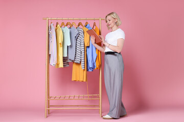 Fashion stylist with tablet and clothing rack on pink background