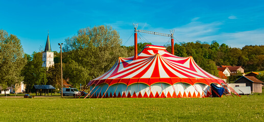 Spring landscape with a red and white circus tent and a church on a sunny day at Postmuenster, Rottal Inn, Bavaria, Germany