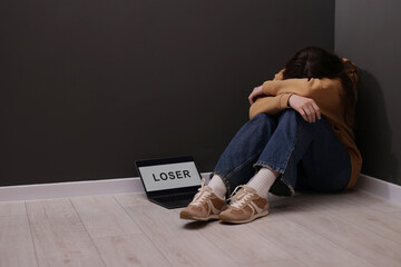 Cyber bullying. Upset teenage girl and laptop with text You Loser on floor indoors. Space for text