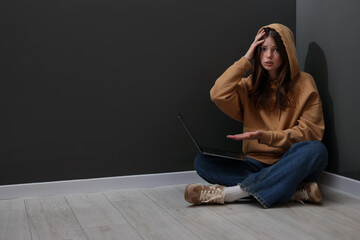 Cyber bullying. Upset teenage girl with laptop on floor indoors. Space for text