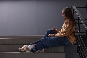 Bullying. Upset teenage girl on stairs indoors. Space for text