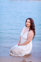 Beautiful brunette girl with long hair in the sea on the shore on the beach in summer