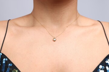 Young woman wearing elegant gold necklace on light grey background, closeup