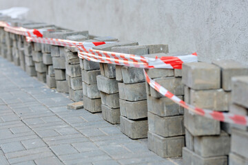 Close view of construction site with removed pavement bricks and hazard tape protecting foundation...