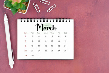 March desk calendar for 2026 year and pen on old red cover. Flat lay.