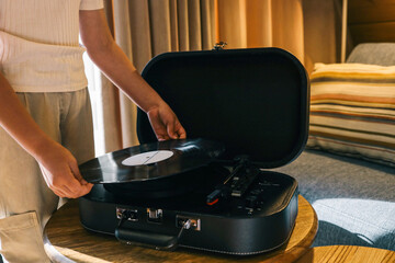 Close-up of young person placing vinyl record on Crosley turntable, cozy indoor setting with soft lighting and striped pillow in background