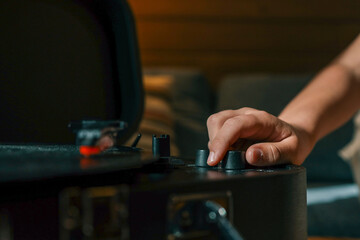 Close-up of hand adjusting volume knob on turntable while vinyl record plays, creating warm...