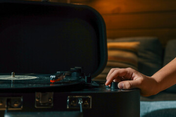 Close-up of hand adjusting volume knob on turntable while vinyl record plays, creating warm...