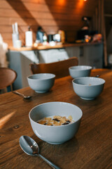 Four bowls of cereal with milk on a wooden dining table in a cozy kitchen interior with soft natural lighting