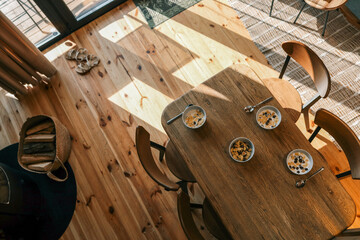 Top view of a cozy breakfast setting with four bowls of cereal and milk on a wooden dining table in natural sunlight