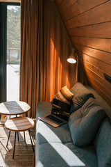 Laptop on a blue couch in a cozy wooden living room with warm natural light, striped pillow, round coffee tables, and a floor lamp near the curtain
