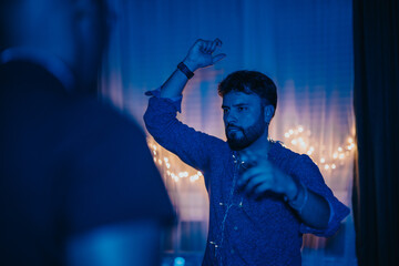 Man dancing under blue light decorations during an evening celebration at home.