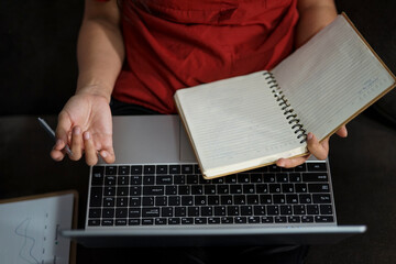 A person is holding a laptop and a notebook
