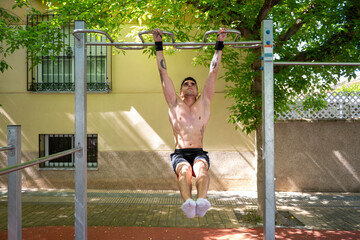 Young man performing calisthenics l sit pull up exercise outdoors