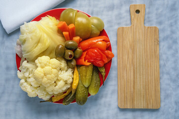 Balkan cuisine. Torshi , mix of different pickled vegetables , in  red plate. Cutting board, copy space