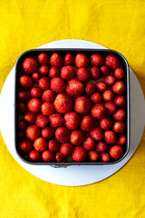 Fresh strawberry in a square springform pan on white round support, yellow tablecloth background.
