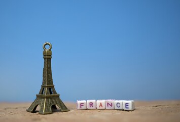 Eiffel Tower Souvenir with France Letter Blocks on a Sand Surface and Clear Blue Sky Background