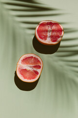 Fresh healthy grapefruit slices on green background with palm leaf shadow. Creative minimal...
