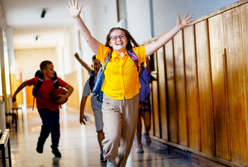 Excited school girl running through hallway with arms outstretched.