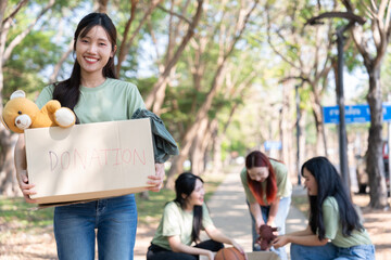 Happy young Asian students diverse volunteers hold donate box and toys for charity to share...