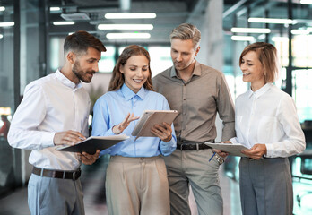 Four business people discussing work together using a tablet in a modern office.