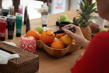 Woman Drawing a Smile on an Orange with a Marker