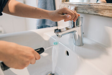 Unrecognizable girl preparing electric toothbrush in the morning, rinsing it under running water