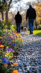 Obraz premium Couple walking dog on sunny path, colorful flowers in foreground.
