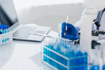 Scientist taking notes during experiment in laboratory. The lab table is filled with test tubes, beakers, and a microscope.
