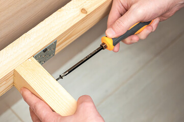 Hands using a screwdriver to secure a wooden frame with a metal bracket