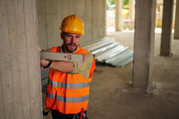 Obraz premium Construction worker wearing a safety helmet and vest, using a spirit level on a concrete pillar in a building under construction, ensuring precise measurements for structural integrity