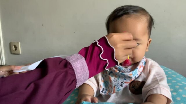 Infant boy learning to eat, being gently spoon-fed by his mother at home. Capturing a sweet bonding moment during a mealtime milestone.