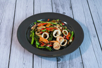 Stir fried noodle with seafood drunken with vegetables and shrimp Squid and seafood in a black bowl Wood plank background