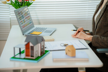 Asian real estate agent in modern office consulting with client, showing property using laptop, mortgage business with house plans, calculator and documents, mortgage and real estate