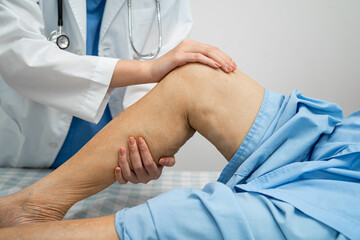 Doctor checking Asian elderly woman patient with scar knee replacement surgery in hospital.
