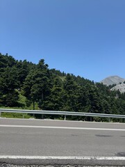 road in the mountains Scenic highway running alongside a dense forest under a clear blue sky....
