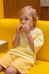 Young child wearing a yellow clothes eats a cheeseburger in a vibrant restaurant, enjoying fast food meal in a casual dining environment. Kids diet, bad food choices, early junk food addiction