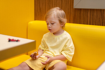 Young child wearing a yellow clothes eats a cheeseburger in a vibrant restaurant, enjoying fast food meal in a casual dining environment. Kids diet, bad food choices, early junk food addiction