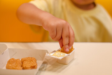 A small child wearing a yellow shirt is eating chicken nuggets in a vibrant environment. Four year old boy enjoying fast food meal. Kids diet, bad food choices, early junk food addiction