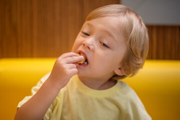 A small child wearing a yellow shirt is eating chicken nuggets in a vibrant environment. Four year old boy enjoying fast food meal. Kids diet, bad food choices, early junk food addiction